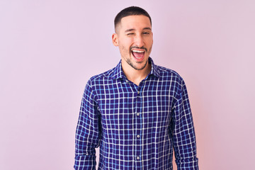 Wall Mural - Young handsome man standing over isolated background winking looking at the camera with sexy expression, cheerful and happy face.