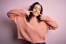 Young Beautiful Woman With Curly Hair Wearing Casual Sweater Over Isolated Pink Background Smiling Cheerful Showing And Pointing With Fingers Teeth And Mouth. Dental Health Concept.