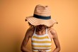 African american tourist woman with curly on vacation wearing summer hat and striped t-shirt with hand on stomach because indigestion, painful illness feeling unwell. Ache concept.