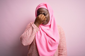 Poster - Young african american plus size woman wearing muslim hijab over isolated pink background tired rubbing nose and eyes feeling fatigue and headache. Stress and frustration concept.