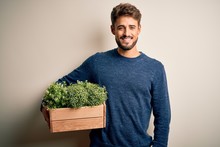 Young Gardener Man With Beard Holding Box With Plants Standing Over White Background With A Happy Face Standing And Smiling With A Confident Smile Showing Teeth