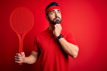 Poster - Young handsome sportsman with beard playing tennis using racket over red background serious face thinking about question, very confused idea