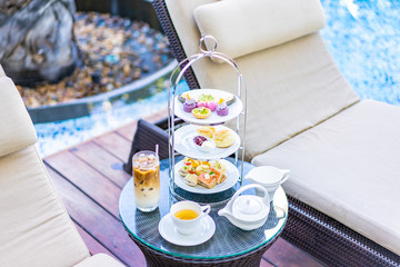 Canvas Print - Afternoon tea set with latte coffee and hot tea on table neary chair around swimming pool