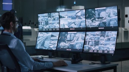 Leinwandbilder - Industry 4.0 Modern Factory: Security Operator Controls Proper Functioning of Workshop Production Line, Uses Computer with Screens Showing Surveillance Camera Footage Feed. High-Tech Security