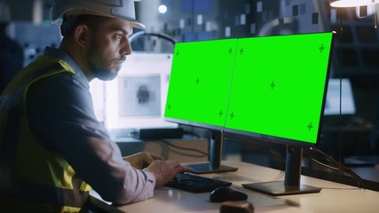 Poster - Engineer Wearing Safety Vest and Hardhat Works on a Computer, Two Monitor Screens Show Chroma Key / Green Screen Displays. Modern High-Tech Industry 4.0 Electronics Production Factory