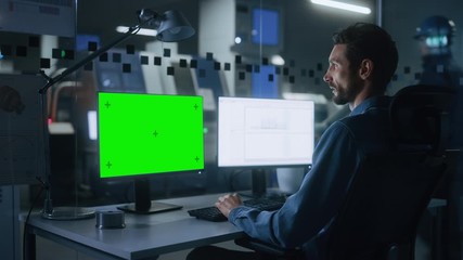 Engineer Works on a Computer, Two Monitor Screens Show Chroma Key / Green Screen and Spreadsheet Software Display. Modern High-Tech Industry 4.0 Electronics Production Factory
