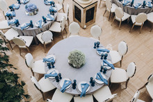 Festive Tables In The Banquet Room Are Decorated With Compositions Of White And Blue Flowers, On The Tables Are Plates With Napkins, Glasses, Candles, A Wedding Dinner