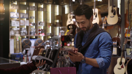 Wall Mural - An upwardly mobile Middle Eastern man using a mobile phone - smartwatch to purchase product at the point of sale terminal in a retail store with nfc identification payment for verification