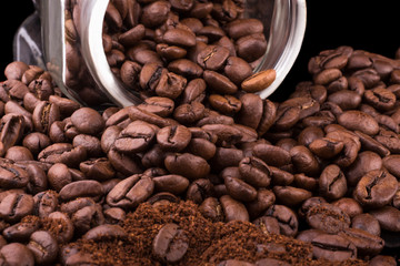 close-up of roasted coffee beans and ground coffee that fell out of the jar on the table on a black background