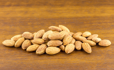 Almonds seeds pour from wood spoon on textured wooden background, top view.