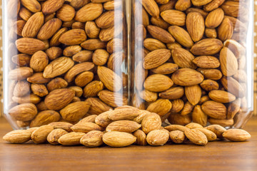 Almonds seeds pour from wood spoon on textured wooden background, top view.