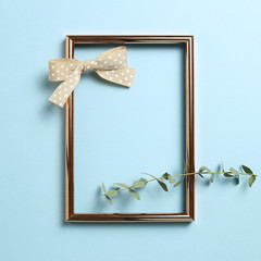 Wall Mural - Empty photo frame with eucalyptus leaves and ribbon on sky blue background. top view, copy space