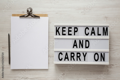 Fotografía 'Keep calm and carry on' words on a modern board, clipboard with blank sheet of paper on a white wooden background, top view
