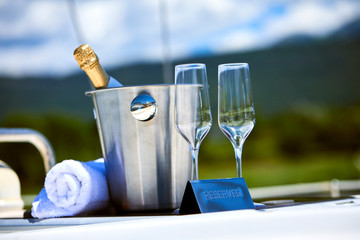 Wall Mural - Romantic luxury evening on cruise yacht with champagne setting. Empty glasses and bottle with champagne and tropical sunset with sea background