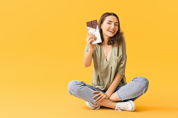 Sticker - beautiful young woman eating tasty chocolate on color background