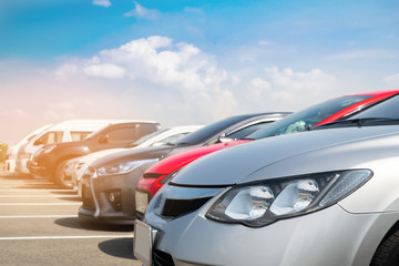 Car parked in large asphalt parking lot in a row with white cloud and blue sky background.