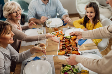 Close-up of senior man serving lunch to his family at dining table.