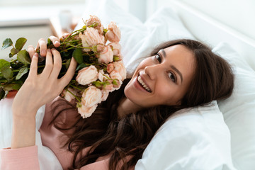 Pretty young woman in bed holding flowers.