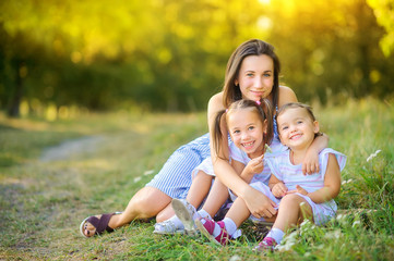 Wall Mural - Happy family. Mom with daughters plays and rests in a beautiful park at sunset, family time.