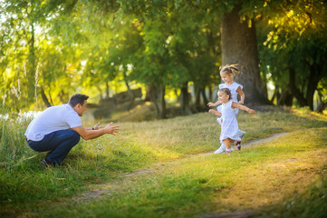 Wall Mural - Happy family. Dad with daughters plays and rests in a beautiful park at sunset, family time.