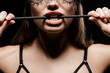 cropped view of seductive woman holding flogging whip in mouth isolated on black