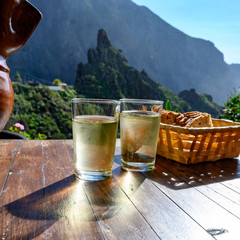 Wall Mural - Man pouring white wine from clay jug into glass on terrace with view on green landscapes of small mountain village Masca on Tenerife, Spain