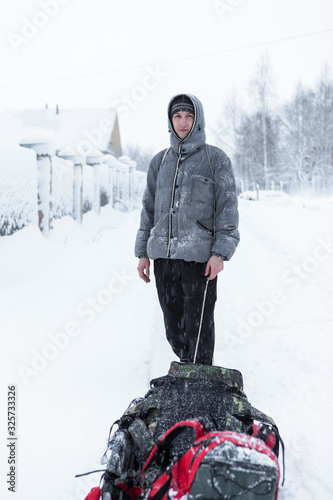 Adult Caucasian man walking with drag sled in the snowy village during strong sn Tableau sur Toile