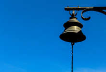 An Old Hanging Metal Bell With Chain In The Blue Sky Background