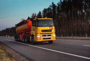 a truck carries a tank of combustible fuel on a highway against a forest and blue sky. the concept o