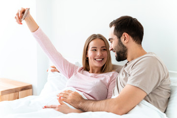 Wall Mural - Portrait of joyful couple hugging and taking selfie photo on smartphone