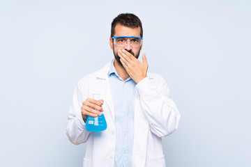 Wall Mural - Young scientific holding laboratory flask over isolated background covering mouth with hands