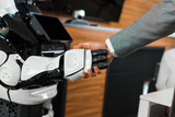 Fototapeta Zachód słońca - partial view of businessman shaking hands with humanoid robot in office