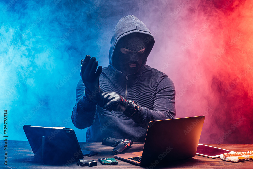 anonymous hacker male sit with laptop over smoky colorful space ...