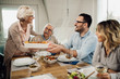 © Drazen - Happy mature woman serving lunch to her family in dining room.