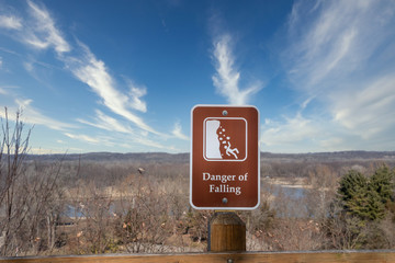 A brown and white sign posted at an overlook warns of the danger of falling.