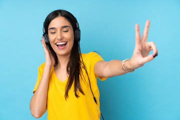 Young brunette woman over isolated blue background listening music and singing