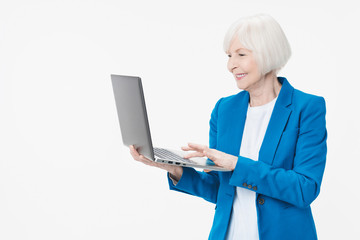 Cheerful mature woman using laptop computer standing isolated over white background