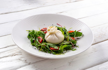 Fresh buratta with salad mix and juicy tomatoes on white wooden background