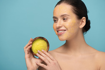 Wall Mural - happy young woman holding wooden bowl with sugar scrub, isolated on blue