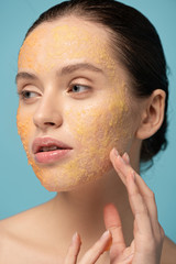 Wall Mural - attractive girl applying yellow sugar scrub on face, isolated on blue