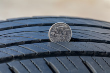 Closeup Of Checking Tire Tread Wear Depth Of Old Tire Using A Quarter Coin. Concept Of Automobile Safety, Maintenance, And Repair