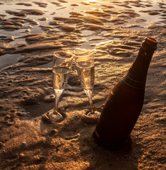 Botella de cava junto a dos copas de cristal en la arena de la playa al atardecer