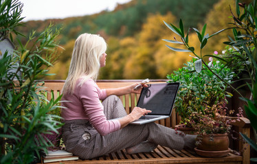 Wall Mural - Senior woman architect with laptop sitting outdoors on terrace, working.