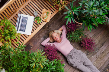 Wall Mural - Top view of senior woman with laptop lying outdoors on terrace, resting.