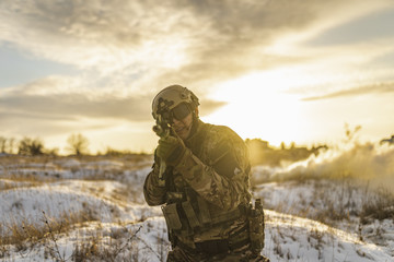 Modern war soldier army Man in camouflage in winter field stands and aiming. commandos with helmet and gun. stands and shooting soldier. sun backlight and smoke. modern warfare. atmosphere of battle