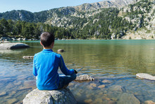 Rear View Of A Boy Sitting On Rock On A Mountain Lake Looking Away