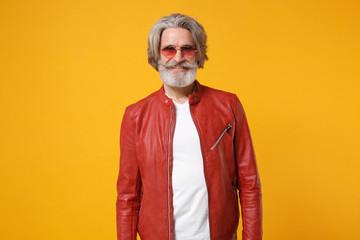 Smiling elderly gray-haired mustache bearded man in red leather jacket, eyeglasses posing isolated on yellow orange background studio portrait. People emotions lifestyle concept. Mock up copy space.