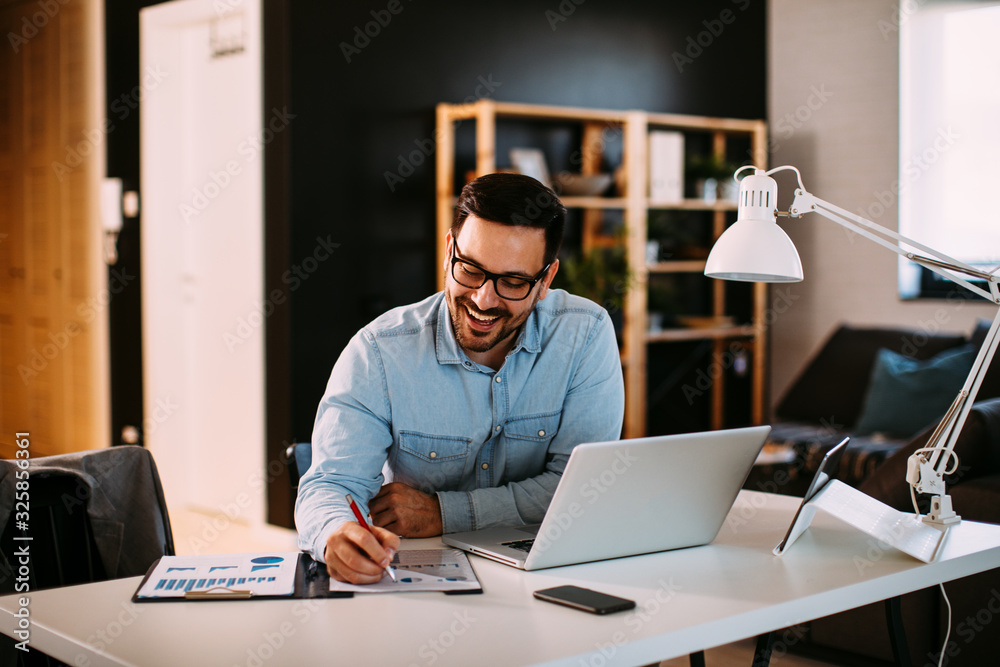 Young business man working at home with laptop and papers on desk - obrazy, fototapety, plakaty 