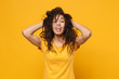 Laughing young african american woman girl in casual t-shirt posing isolated on yellow orange background in studio. People lifestyle concept. Mock up copy space. Having fun holding hands behind head.