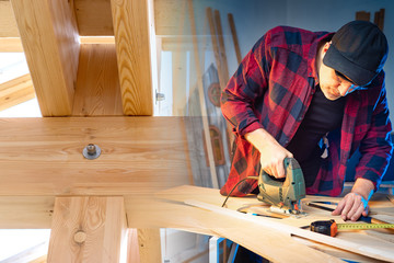Poster - Work in a carpentry workshop. A man works with an electric jig saw. A man is sawing parquet. Wood processing. Work in the furniture workshop. Furniture manufacturing. Concept - Construction Tools